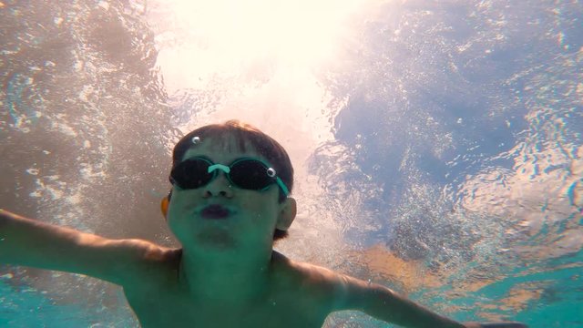 From inside the pool 5-year-old boy jumps into the pool and dives with swimming goggles. It's summer time in a sunny blue cloudy day.