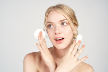 Obraz na płótnie Canvas A blonde with bare shoulders holds cotton pads near her face skin care light background