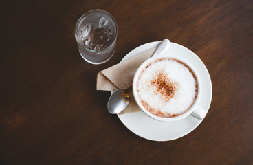Close-up of hot coffee on white coasters with a glass of water with ice cubes on wooden table.