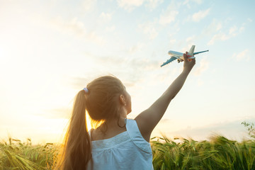 Little girl holding airplane toy in the green wheat field