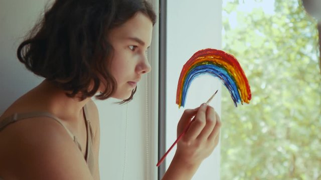 kid girl at home on the window draws a rainbow during coronavirus Covid-19 the quarantine period on self-isolation. Stay at home social media share lifestlye. daughter child pandemic creative