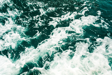 Dark turquoise sea water with white foam texture on the surface. Background image.