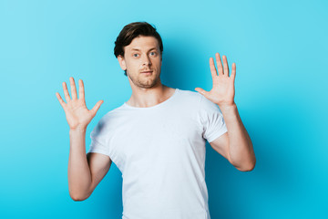 Naklejka premium Confused man in white t-shirt looking at camera on blue background