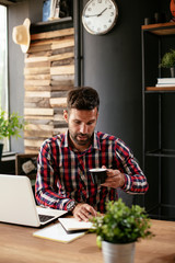 Young businessman drinking coffee in office. Businessman sitting at office desk working on laptop computer...