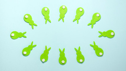 Fototapeta premium Green rabbits bunnies converge and diverge on blue background with copy space in centre of the frame. Flat lay top view. Easter concept.