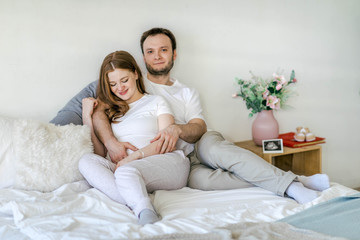 Family waiting for the baby. Husband and pregnant wife in a bright interior hug and smile....