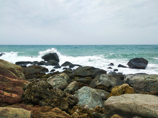 Fototapeta na wymiar white waves hit the rocks on the sea shore in cloudy day