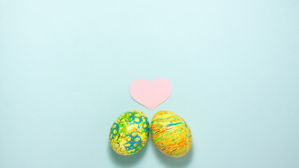 Fototapeta na wymiar Two easter colorful eggs roll out to each other on blue background. Flat lay with copy space
