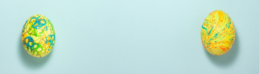 Banner of yellow and green easter eggs at the left and right on blue background. Flat lay top view with copy space.