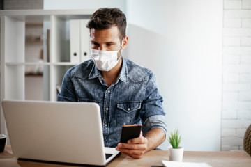 Businessman with medical mask in office. Handsome man using the phone at work..