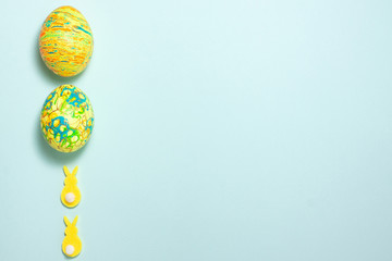Yellow rabbits and green easter egg on the left side on blue background. Flat lay top viiew with copy space