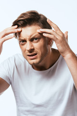 Worried man touching skin on forehead and looking at camera isolated on white