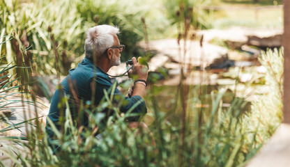 60 year old man in harmony with nature, taking pictures on the lake. Senile depression and loneliness.