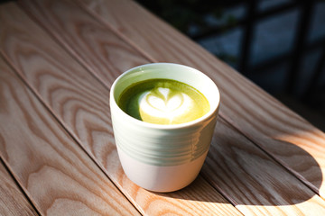A cup of green tea matcha latte on wooden background at cafe. Healthy food concept. Sunny day. Side view. Close-up.
