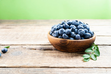 Fresh blueberry in wooden bowl. Juicy and fresh blueberries with green leaves on rustic table. Concept blueberry antioxidant for healthy eating and nutrition. Copy space