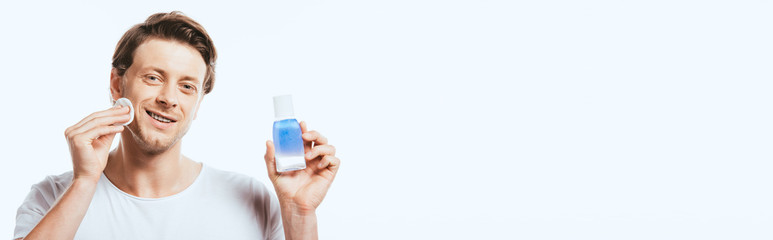 Panoramic crop of young man applying toner with cotton pad isolated on white