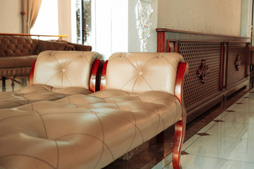 Rich vintage mahogany sofa with cream leather upholstery stands next to a large mirror. Hall interior in retro, classic style. The concept of furniture stores and their manufacture.