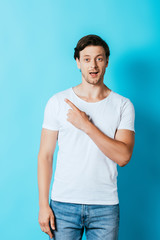 Excited man in white t-shirt looking at camera while pointing with finger on blue background