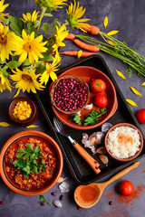Mexican spicy food with beans, corn, tomatoes and chili, boiled rice, paprika on a dark wooden background. View from above. Still life with sunflowers