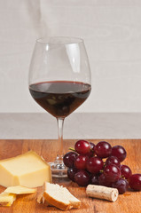 front view, close distance of a glass of French red wine with a bunch of freshly picked, local, ripe grapes with a slice of cheese, cracker and wine cork
