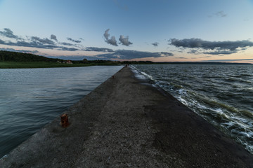 Stone pier inbetween calm and stormy waters.