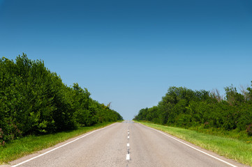suburban empty road asphalt surrounded by trees and grass. The concept of transportation and travel. Background green grass asphalt and blue sky