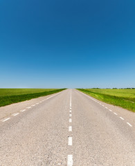 suburban empty road asphalt surrounded by trees and grass. The concept of transportation and travel. Background green grass asphalt and blue sky