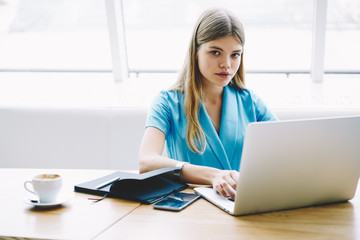 Portrait of professional manager sitting with notepad and laptop device connecting to wireless...