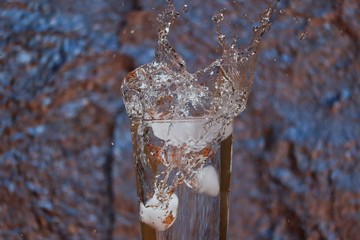 Naklejka na ściany i meble Amazing Water Splash from Glass with Ice Cubes in front of Tinfoil. Summer Vibes with Ice Cubes Falling into Water.