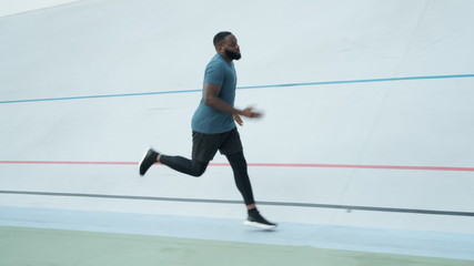 Fototapeta na wymiar Young man running on sport track at stadium. Active athlete jogging outdoors
