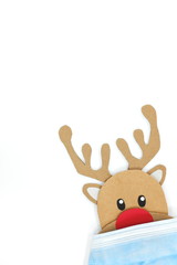 Cardboard cutout of Rudolph the red-nosed reindeer peeking while wearing a face mask. Covid during Christmas season concept. White background, portrait, with copy space.