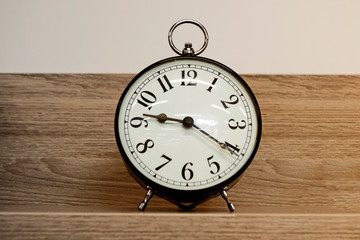 Alarm clock. White background and black arrows. A wooden shelf.