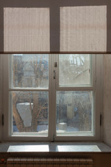 Dirty window with raised fabric shutters, outside is spring