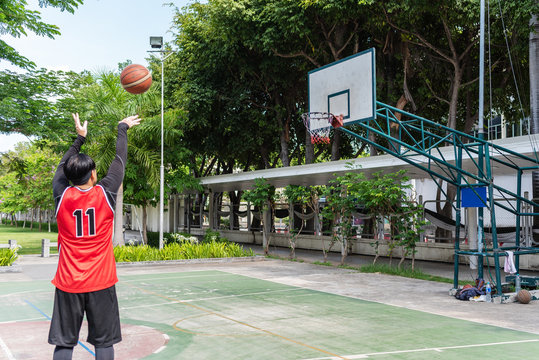 Asian basketball man is shooting ball to the hoop at the court. In which this picture focus to the basketball hoop