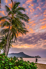 Sunrise over Waikiki beach with palm trees and diamond head in background.