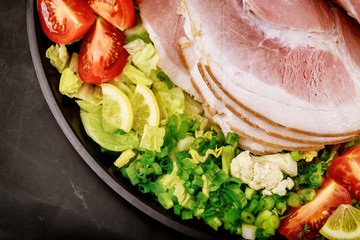 Ham with chopped vegetables on black plate.
