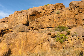 Looking up at massive rock formation, withits changing shape, lines and design, rich in rusy sandstone color against a blue sky, adds to the definition and character of this desert scene-Joshua Tree