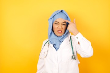 Young arab doctor woman wearing medical uniform standing over yellow background  pointing unhappy...