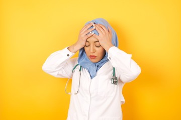Young arab doctor woman wearing medical uniform standing over yellow background  suffering from strong headache desperate and stressed because of overwork. Depression and pain concept.