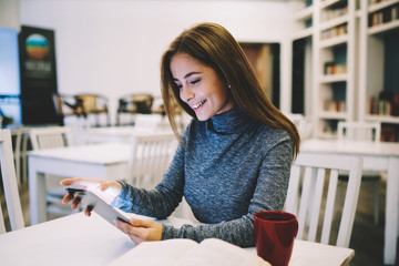 Cheerful hipster girl reading funny story and messaging with friends in online chat via modern...