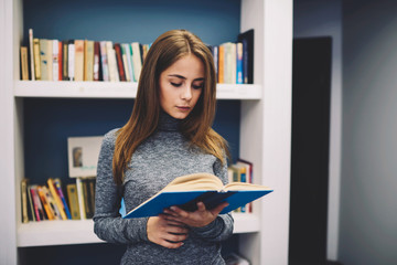Smart young female journalist focused on interesting book with existing poems of talented author...