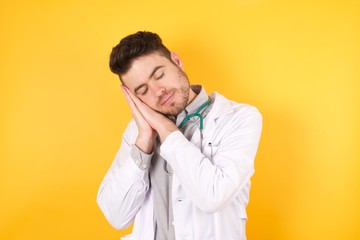 Young handsome Caucasian doctor man wearing medical uniform and stethoscope sleeping tired dreaming and posing with hands together while smiling with closed eyes.