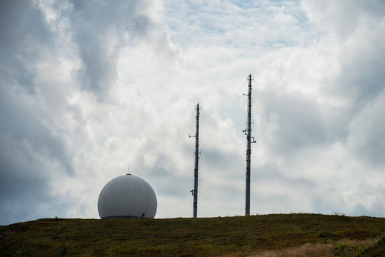 view of radar in a sphere and big antena on the top of the mountain on cloudy sky background