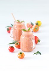 Vegetable smoothie of yellow, orange and red fresh tomatoes in a glass jar with a bamboo straw on a light background