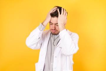 Young handsome Caucasian doctor man wearing medical uniform suffering from strong headache desperate and stressed because of overwork. Depression and pain concept.