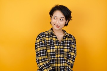 Photo of amazed  Young asian woman with short hair wearing plaid shirt standing over yellow...