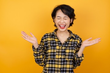 Emotive Young asian woman with short hair wearing plaid shirt laughs loudly, hears funny joke or story, raises palms with satisfaction, being overjoyed, amused by friend over white background. 