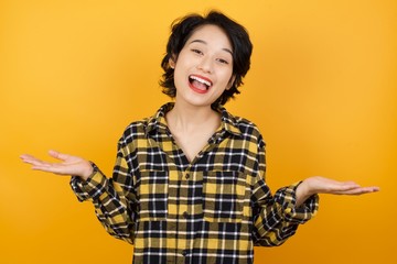 Young asian woman with short hair wearing plaid shirt standing over yellow background celebrating crazy and amazed for success with arms raised and open eyes screaming excited. Winner concept