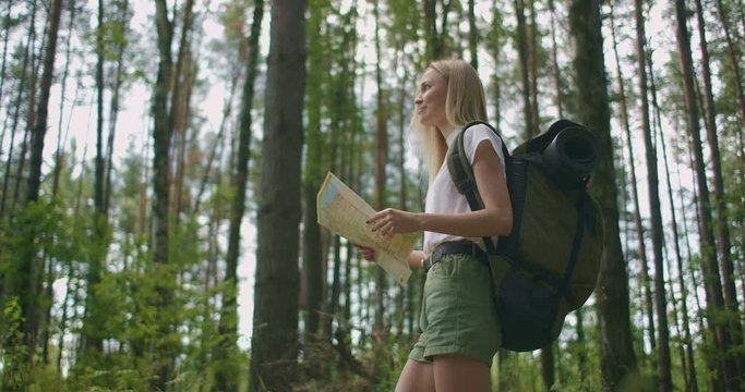 Young caucasian woman looking for direction on a map while hiking in the forest. Happy girl while hiking in nature and orienteering with help of a map