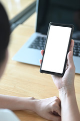Cropped image of the hand is using a white blank screen mobile at the wooden table.